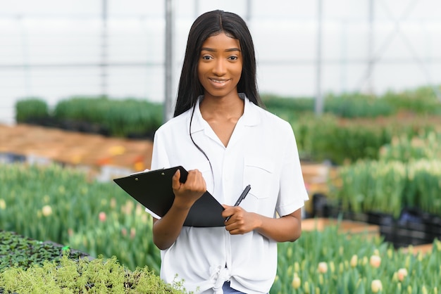 Mooie jonge lachende Afro-Amerikaanse meisje, werknemer met bloemen in kas.