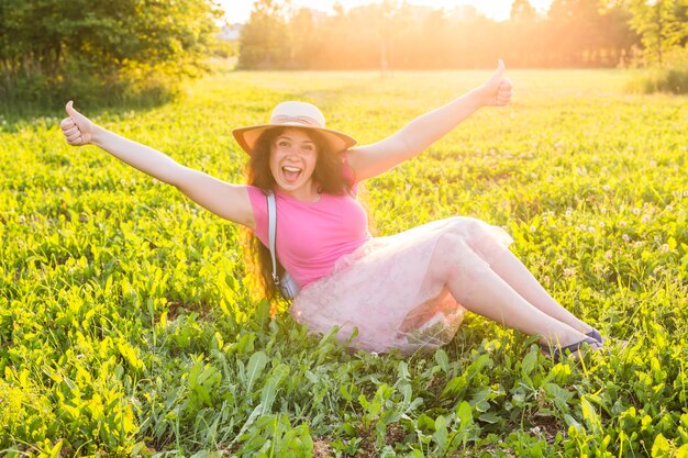 Mooie jonge lachende ondeugende vrouw die op het gras zit en glimlacht