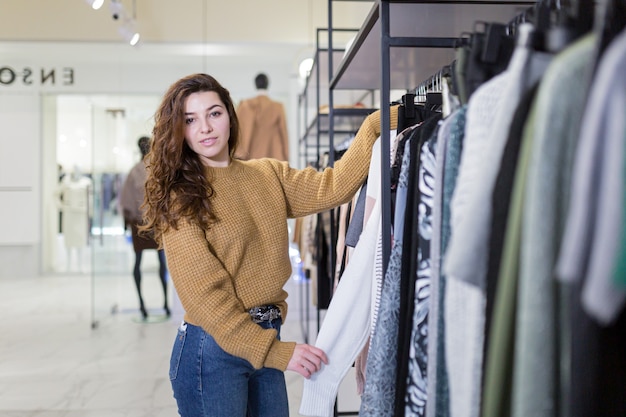 mooie jonge lachende vrouw gaat winkelen en kiest kleding in de winkel tijdens kortingen en verkoop