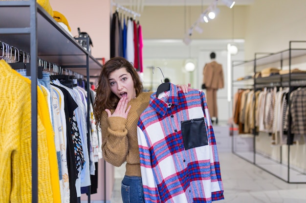 mooie jonge lachende vrouw gaat winkelen en kiest kleding in de winkel tijdens kortingen en verkoop