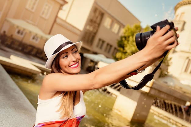 Mooie jonge lachende vrouw met hoed selfie te nemen op het stadsplein naast de fontein.