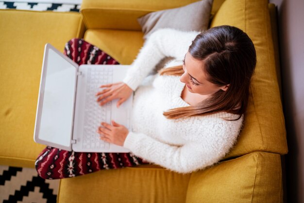 Mooie jonge lachende vrouw ontspannen op de bank in de woonkamer en het gebruik van laptop. Bovenaanzicht.