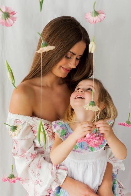 Mooie jonge langharige moeder met dochtertje van 3 jaar oud met gekleurde bloemen op witte achtergrond Mothers Day Holidays Gelukkig kind