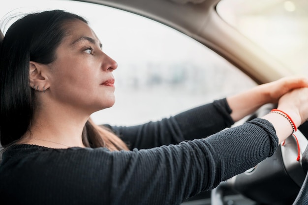 Mooie jonge latijnse vrouw die in de auto zit met haar handen aan het stuur en zorgvuldig naar de horizon kijkt