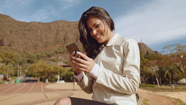 Mooie jonge latijnse vrouw die smartphone gebruikt die zich op stadsstraat bevindt portret van latina glimlachende vrouw die mobiele telefoon gebruikt