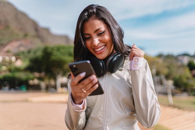 Mooie jonge Latijnse vrouw die smartphone gebruikt die zich op stadsstraat bevindt