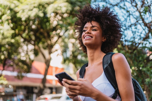 Mooie jonge Latijnse vrouw die smartphone gebruikt die zich op stadsstraat bevindt