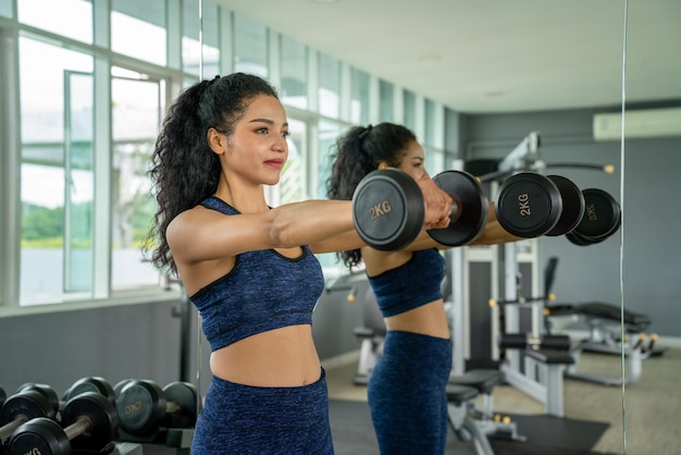 Mooie jonge meisje krachttraining met halters op sportschool Sport gezonde levensstijl Atletische vrouw neemt halters krachttraining Jonge vrouw training gezonde levensstijl Sport vrouw fit spier