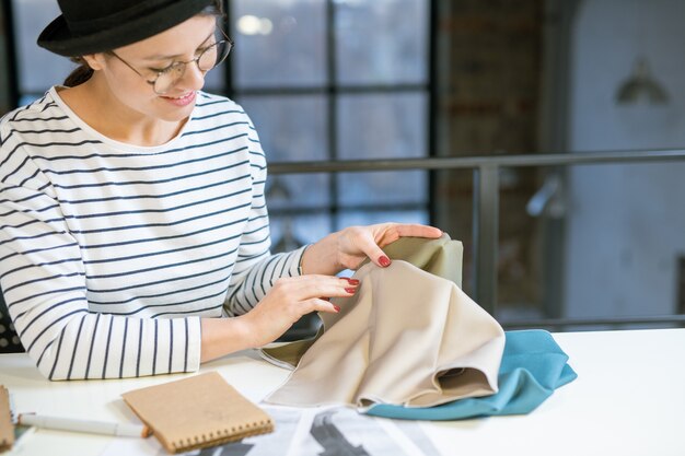 Mooie jonge modeontwerper kijken naar stuk textiel tijdens het kiezen van stof voor nieuwe collectie in de studio