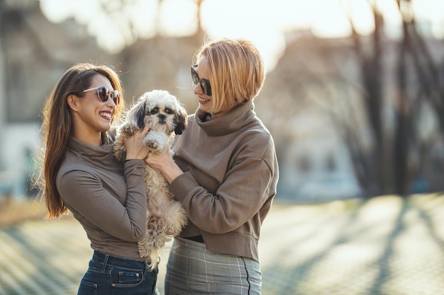 Mooie jonge modevrouwen brengen tijd door met hun schattige hondje spelen, spelen in de stadsstraat.