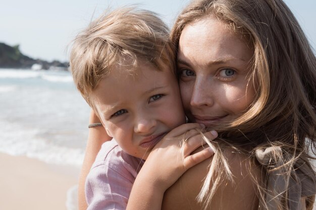 Mooie jonge moeder en zoon knuffelen op het strand in zonnige zomerdag