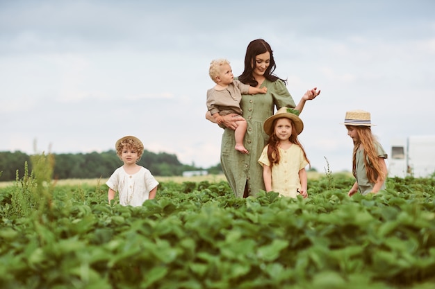Mooie jonge moeder met kinderen in een linnen jurk met een mandje aardbeien verzamelt een nieuwe oogst en heeft plezier met de kinderen