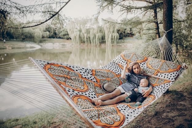 Mooie jonge moeder rustend op hangmat in de buurt van een meer met haar kleine kind familie vakantie concept moeder en zoon op een kampeertrip