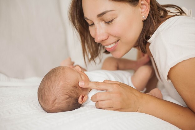 Mooie jonge moeder speelt met de baby in bed. Moederschap.