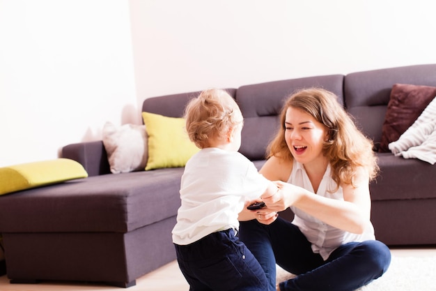 Mooie jonge moeder speelt met haar baby op de vloer. Moeder en haar zoon hebben samen plezier in hun huis