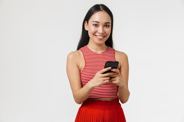 mooie jonge mooie Aziatische gelukkige vrouw poseren geïsoleerd over witte muur met behulp van mobiele telefoon.