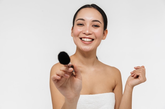 mooie jonge mooie Aziatische vrouw met een gezonde huid poseren naakt geïsoleerd over witte muur met make-up borstel.