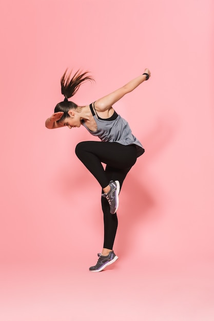 mooie jonge mooie fitness vrouw die loopt, maakt sportoefeningen geïsoleerd over roze muur