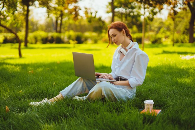 Mooie jonge mooie roodharige vrouw in park buiten met behulp van laptopcomputer voor studie of werk online...