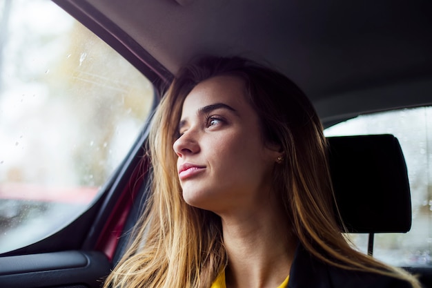 Mooie jonge onderneemsterzitting op achterbank van een auto en kijkend buiten het venster