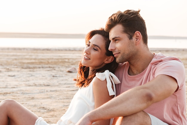 Mooie jonge paar dragen zomerkleding ontspannen op een deken op het strand, knuffelen