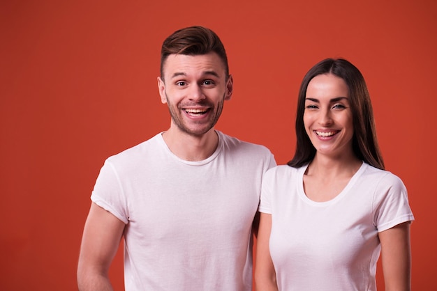 Mooie jonge paar in witte lege t-shirts poseren op oranje achtergrond. Relatie, familie, reclame