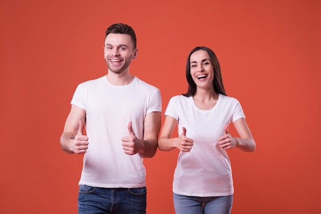 Mooie jonge paar in witte lege t-shirts poseren op oranje achtergrond. Relatie, familie, reclame