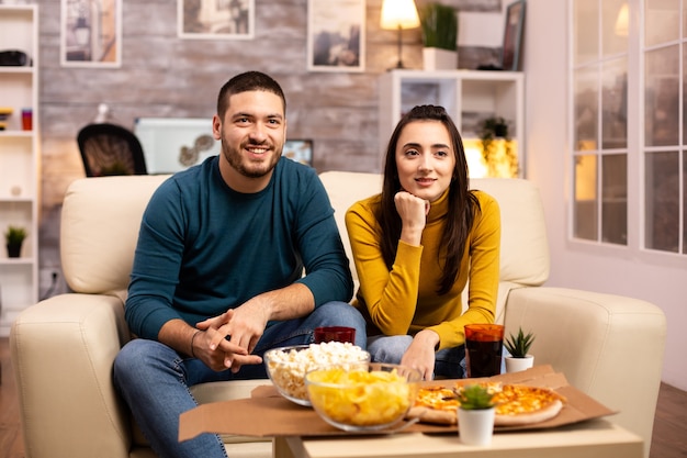 Mooie jonge paar tv kijken en fast food afhaalmaaltijden eten in de woonkamer