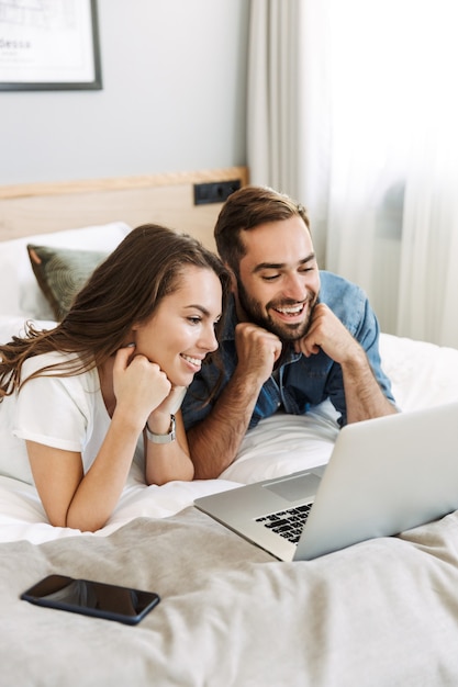 Mooie jonge paar verliefd thuis, liggend in bed, kijken naar laptopcomputer