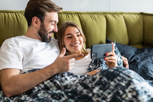 Mooie jonge paar verliefd thuis tot in bed, met behulp van mobiele telefoon