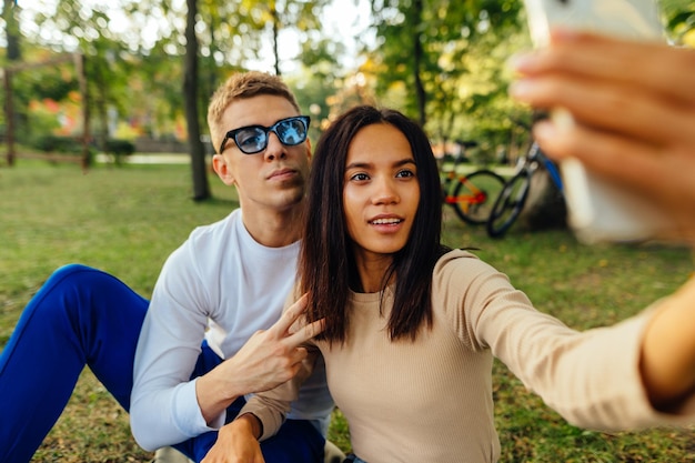 Mooie jonge paar zittend op het grasveld in het park en het nemen van een selfie op een smartphone