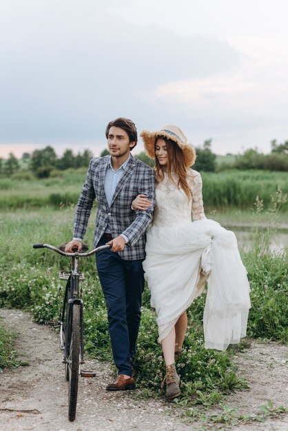 Mooie jonge paarbruid en bruidegom die op een gebied met een fiets lopen