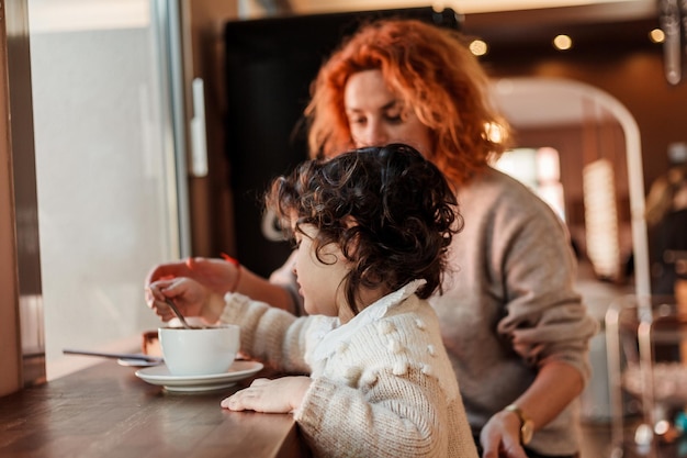 Mooie jonge roodharige moeder met schattige dochter met krullend haar zitten in een gezellig café en drinken hete school Mothers Day Warm