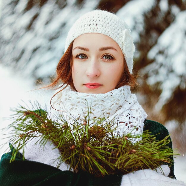 Mooie jonge roodharige vrouw in groene trui en witte trouwjurk wandelen in ijzig winterpark