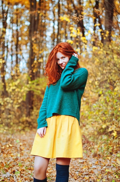 mooie jonge roodharige vrouw met sproeten, blauwe ogen in kleurrijk herfstpark. Groene trui. Val