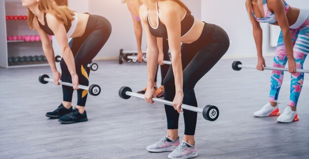 Mooie jonge sportenvrouwen die spieren met domoren in gymnastiek oppompen.