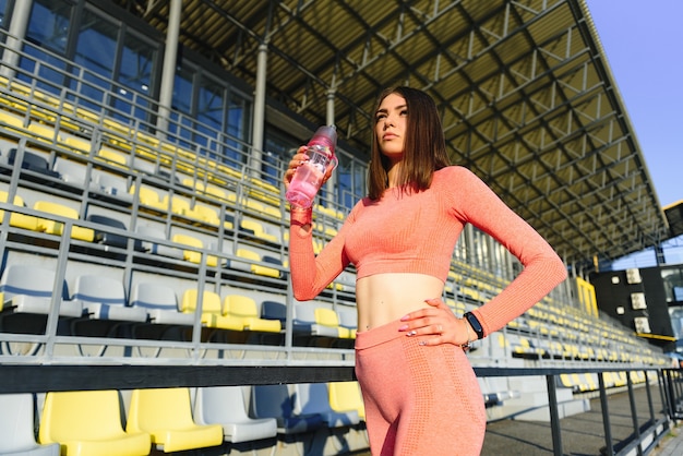 Mooie jonge sportieve vrouw drinkwater na het hardlopen. Fit joggermeisje dat een pauze neemt na het sporten. Lifestyle, mensen, sport en vrije tijd concept.