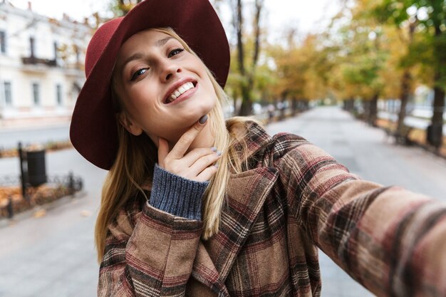 Mooie jonge stijlvolle blonde vrouw draagt een jas buiten wandelen, een selfie te nemen