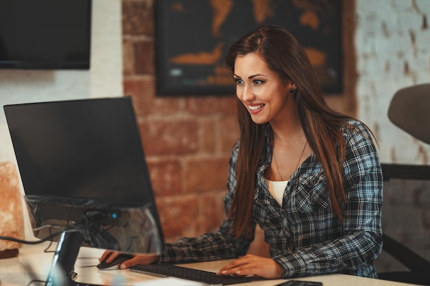 Mooie jonge succesvolle lachende vrouw analyseert nieuw project op haar computer op kantoor.