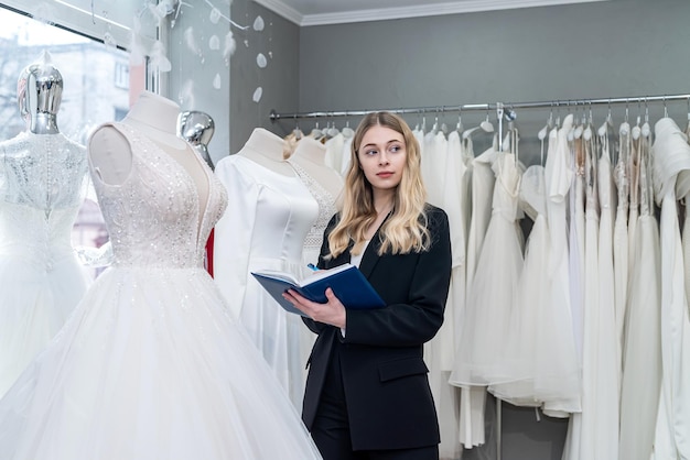 Mooie jonge verkoopster houdt notities dagboek in moderne trouwwinkel Vrouwelijke bruidswinkel