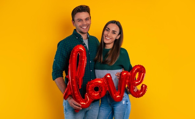 Mooie jonge verliefde paar vieren Valentijnsdag met romantische ballon in handen, knuffelen elkaar en lachen samen terwijl ze geïsoleerd op gele achtergrond