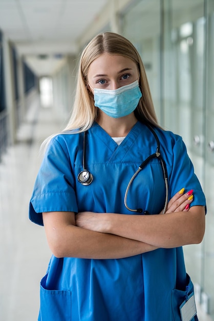 Mooie jonge verpleegster met een masker staat in de gang