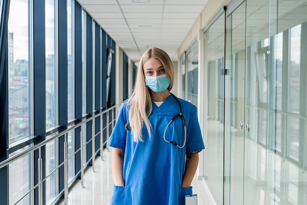 Mooie jonge verpleegster met een masker staat in de gang