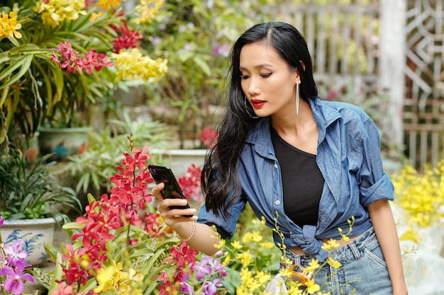 Mooie jonge vietnamese vrouw die foto's maakt van prachtige bloemen in een kas voor sociale media