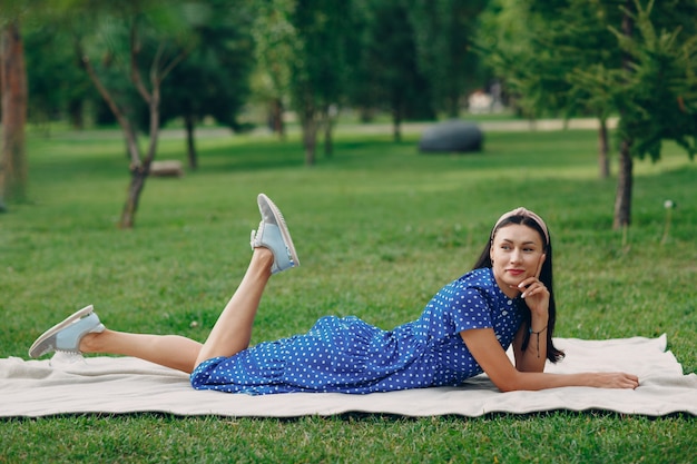 Mooie jonge volwassen vrouw in blauwe jurk picknick op weide in park.