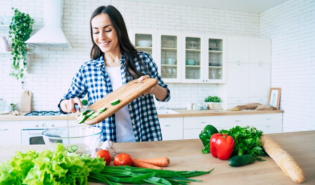 Mooie jonge vrouw bereidt groentesalade in de keuken. Gezond eten. Veganistische salade. Eetpatroon. Dieetconcept. Gezonde levensstijl. Thuis Koken. Eten koken. Ingrediënten snijden op tafel