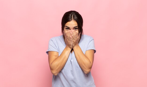 Mooie jonge vrouw blij en opgewonden, verrast en verbaasd mond bedekt met handen, giechelend met een schattige uitdrukking