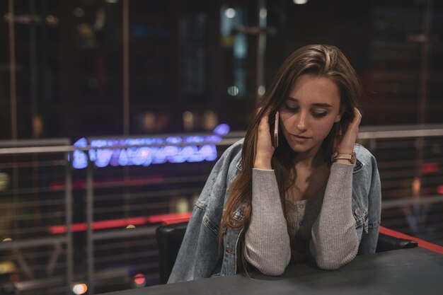 Mooie jonge vrouw die aan de telefoon praat terwijl ze's nachts op tafel zit.