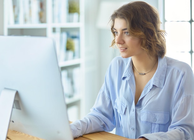 Mooie jonge vrouw die aan het bureau zit en op laptop typt