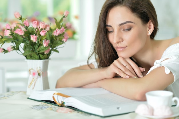 Mooie jonge vrouw die aan tafel zit en een interessant boek leest